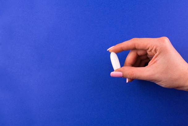  One suppository for anal or vaginal use in a female hand on a blue background. Medical candles. Copy space. - Foto, afbeelding