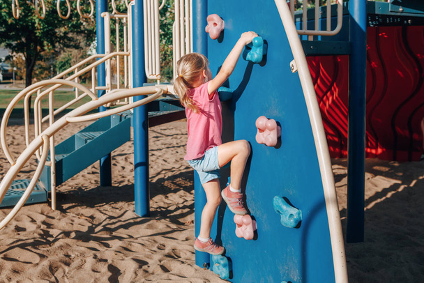 Pequena menina pré-escolar escalando parede de rocha no playground fora o
 - Foto, Imagem