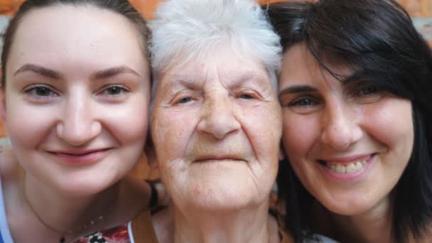 Портрет літньої жінки з дочкою та онукою, яка дивиться в камеру та посміхається разом. Щасливі жінки демонструють радісні емоції на обличчях. Позитивна експресія обличчя жінок. крупним планом
 - Кадри, відео