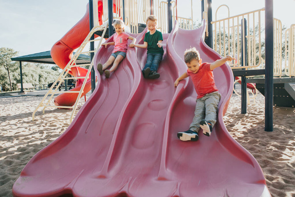 Aktywny szczęśliwy biały dzieci przesuwne na placu zabaw szkolnych - Zdjęcie, obraz