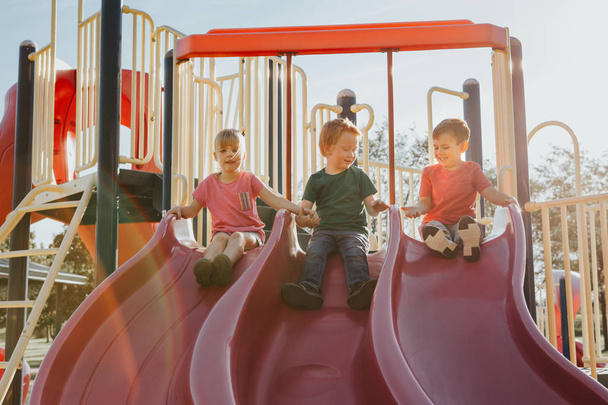 Active happy Caucasian children sliding on playground schoolyard - Fotoğraf, Görsel