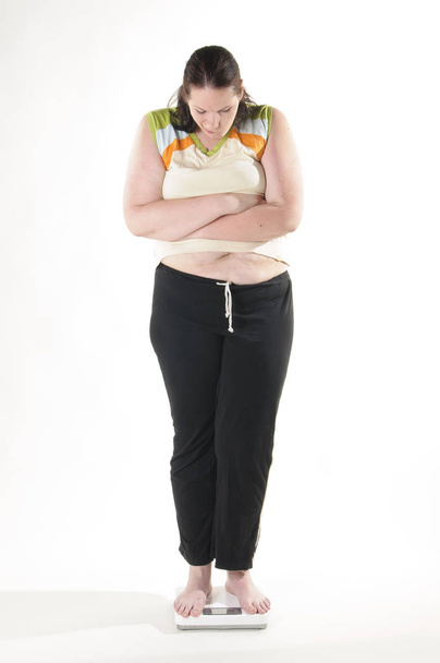 obese adult woman with long black hair standing on the scales and is appalled by their weight,against white background. - Zdjęcie, obraz