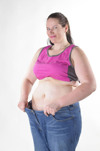 adult overweight woman has already lost a lot of weight and showing her to big pants against white background. - Photo, image