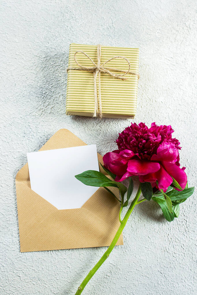 Mothers day or Womens day concept. Burgundy peony and empty note card for text on concrete background. Top view, flat lay, copy space - 写真・画像