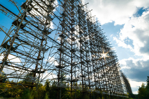 Sovětský za horizontem radarové sítě kovové konstrukce v kontaminované černobylské vylučovací zóně. Vertikální obraz se sluneční erupcí za radarem. Obrázek pozadí. 2019.10.08. - Fotografie, Obrázek