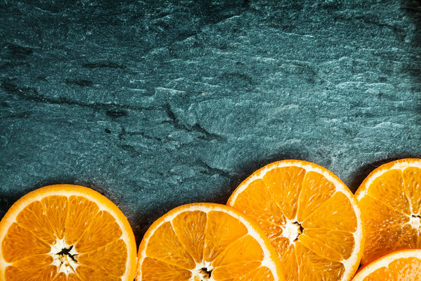 Border of colorful fresh juicy orange slices on a textured slate background with copyspace and vignetting - Photo, image