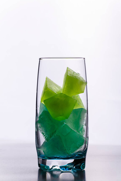 glass of green cocktail with ice cubes on white background - 写真・画像