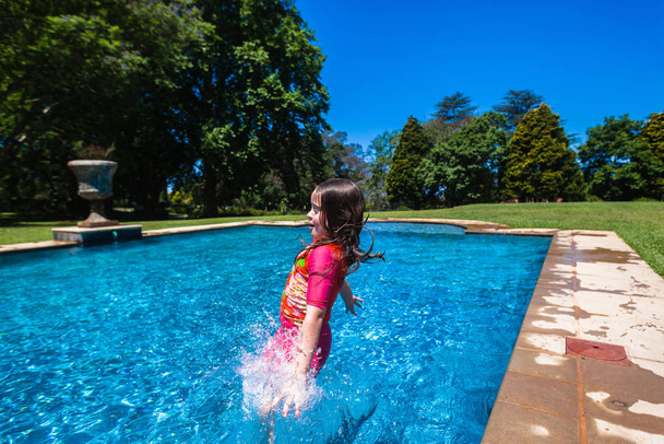 Girl at home playtime jumping into swimming pool outdoors summer - Φωτογραφία, εικόνα