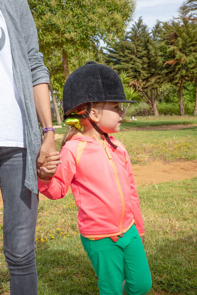 menina com equitação cap segurando mão de mãe esperando para ri
 - Foto, Imagem