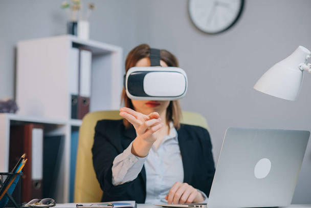 Modern business woman wearing virtual reality glasses in office. Young girl using VR goggles in office. Pretty woman working in augmented reality at workplace - Foto, immagini