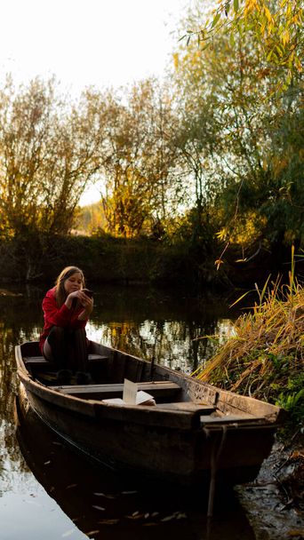 göndör lány ül a szélén egy elhagyatott fa csónak naplementekor. - Fotó, kép