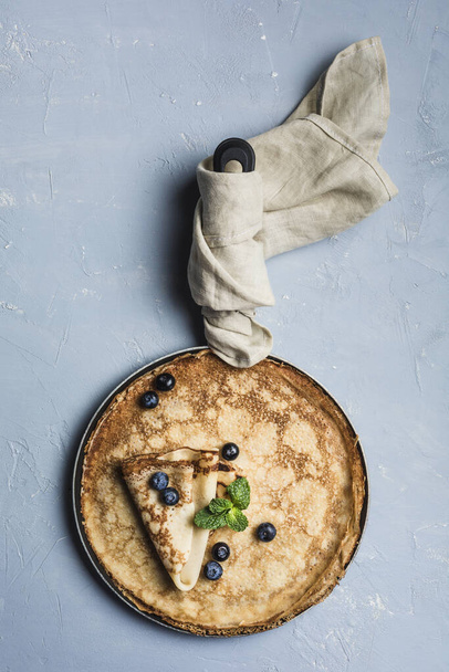 Unas tortitas en una sartén con arándanos y menta en un blu claro
 - Foto, Imagen