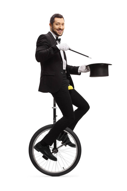 Magician with a wand riding a unicycle and smiling at camera  - Φωτογραφία, εικόνα