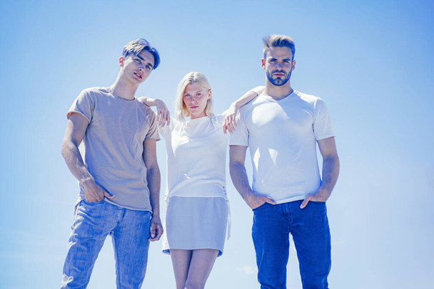 Two handsome men and girl standing between them look down at camera at clear blue sky background. Company of best friends get upset because of bad news. - Foto, afbeelding