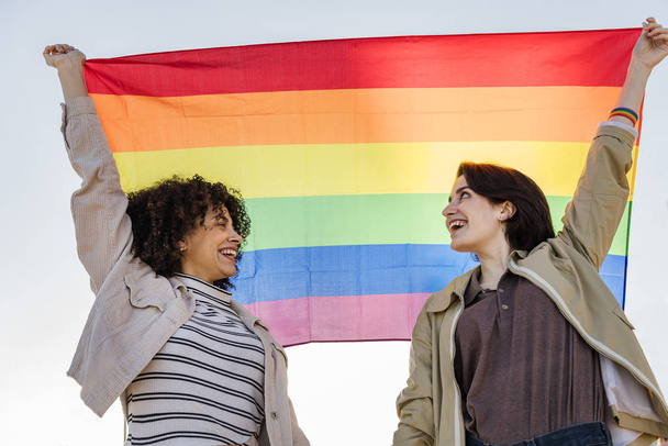pár mosolygó nő felemeli a szivárvány zászlót - Fotó, kép