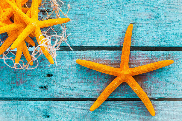 Collection of orange starfish on turquoise blue wooden boards with fishing net for a colourful nautical or marine background with copyspace - Foto, imagen