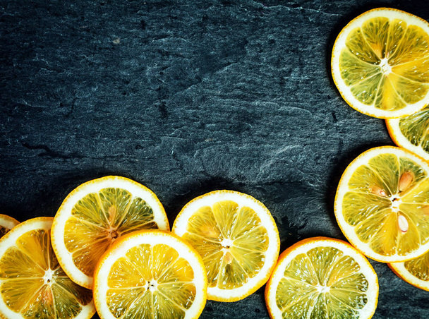Orange slices arranged in a corner decoration on a dark grey textured slate background with copyspace for your text - Photo, Image