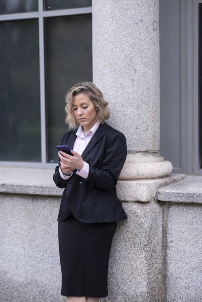 short curly hair blonde woman dressed as executive interacting with her phone - Фото, зображення