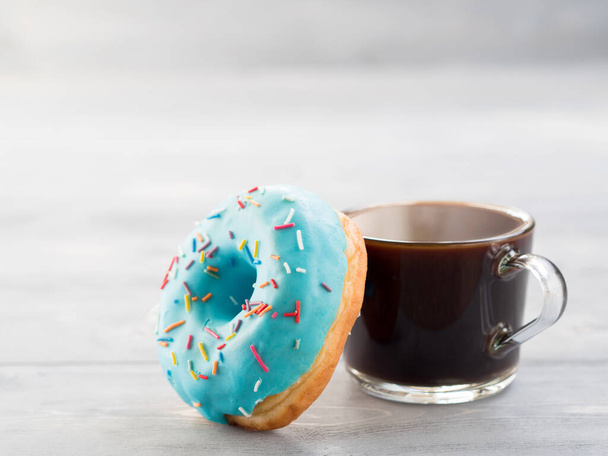 Blue donut and coffee on gray wooden background with copy space. Glazed doughnut and coffee cup on grey wooden table with copyspace - Fotografie, Obrázek