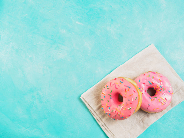 Top view of two pink donuts on blue concrete background with copy space. Colorful donuts with copyspace. Glazed doughnuts with sprinkles - Photo, Image