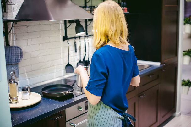 blonde woman with a pot in the kitchen. housewife in apron has been cooking in the kitchen, put pots and pans on the hob - Φωτογραφία, εικόνα