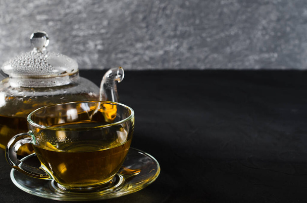 Cup of delicious herbal tea and glass teapot on dark background. Copy space - Foto, afbeelding
