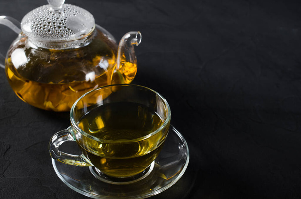 Cup of delicious herbal tea and glass teapot on dark background. Copy space - Foto, Imagem