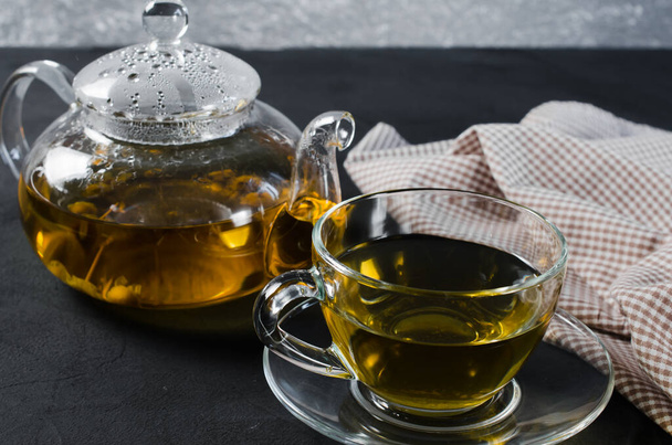 Cup of delicious herbal tea and glass teapot on dark background. Copy space - Foto, imagen