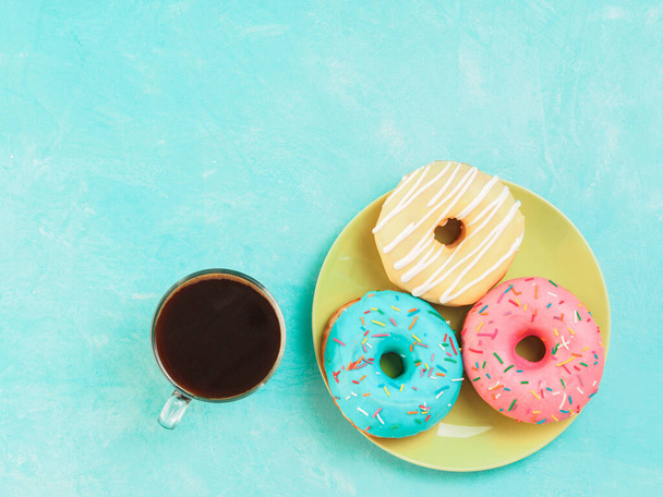 Top view of assorted donuts and coffee on blue concrete background with copy space. Colorful donuts on plate and coffee background. Various glazed doughnuts with sprinkles. - Photo, Image