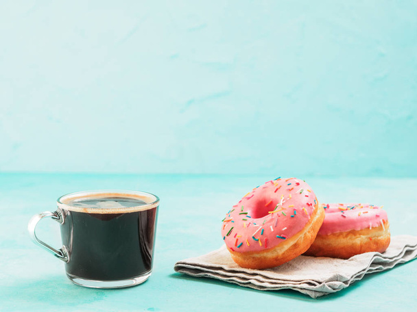 Two pink donuts and coffee on blue concrete background with copy space. Colorful donuts and coffee cup with copyspace. Glazed doughnuts with sprinkles - Photo, Image