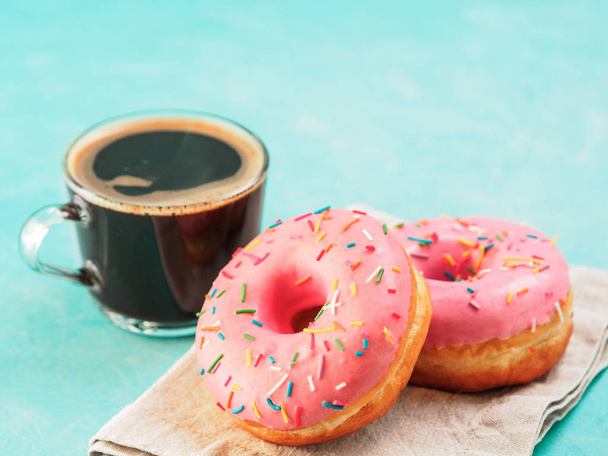 Two pink donuts and coffee on blue concrete background with copy space. Colorful donuts and coffee cup with copyspace. Glazed doughnuts with sprinkles - Photo, image