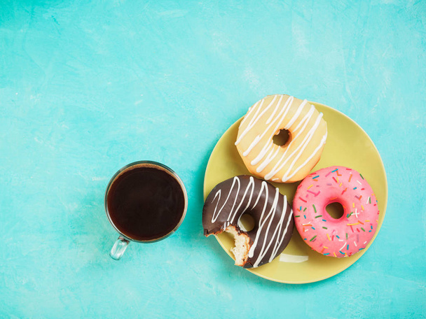 Top view of assorted donuts and coffee on blue concrete background with copy space. Colorful donuts on plate and coffee background. Various glazed doughnuts with sprinkles. - Photo, Image