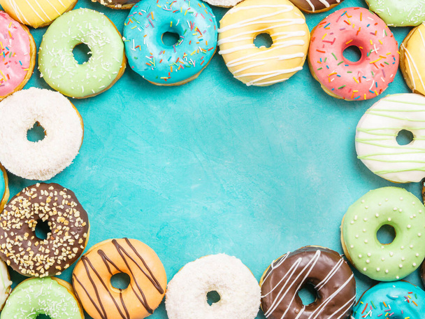 Top view of assorted donuts on blue concrete background with copy space. Colorful donuts background. Various glazed doughnuts with sprinkles. - Фото, изображение