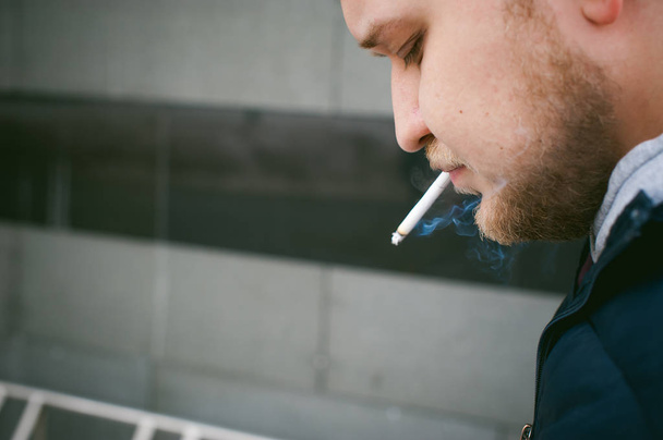 Portrait of a man with a beard with a mustache, smoking a cigarette, with an emotional face in the open air - Photo, image
