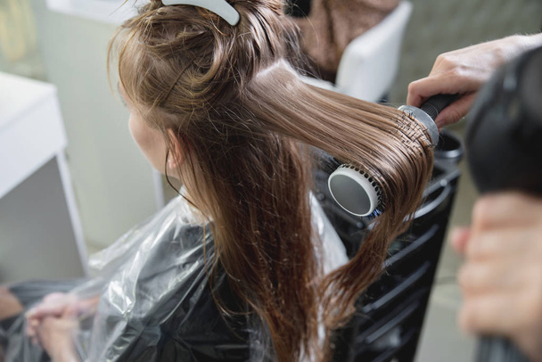 Close up of hairdressers hands drying long blond hair with blow dryer and round brush - Fotó, kép