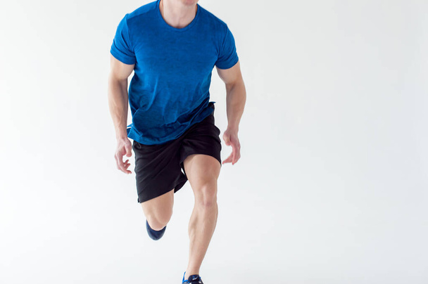 Running man on low start. Stands in rack, ready to achieve goals and wins. Young sexy Muscular male athlete wearing sporty blue t-shirt and shorts, studio portrait white background.Motivation concept - Photo, Image