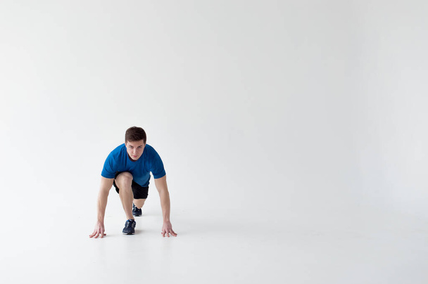Running man on low start. Stands in rack, ready to achieve goals and wins. Young sexy Muscular male athlete wearing sporty blue t-shirt and shorts, studio portrait white background.Motivation concept - Foto, afbeelding