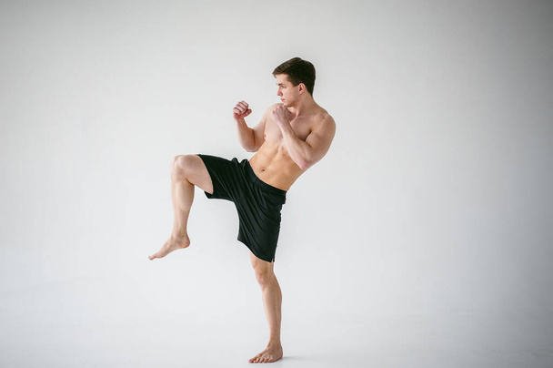 young sexy handsome men strong Athlete's body with bare torso, Dressed black sports shorts, portrait of studio of light-skinned strong man standing in fighting stance Kicking, straining powerful legs - Photo, Image