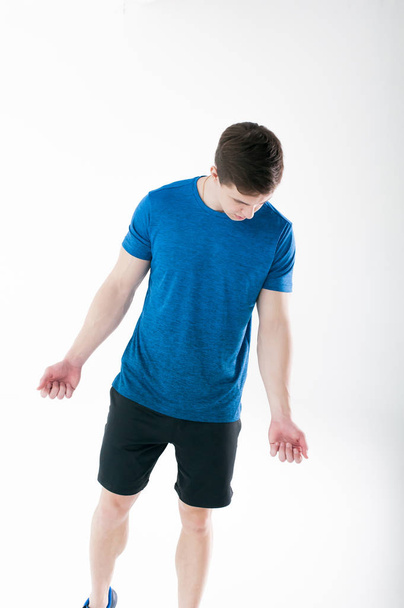 Young muscular handsome athletic man dressed in blue sport shirt, shorts and sneakers standing on white background in studio - Foto, afbeelding