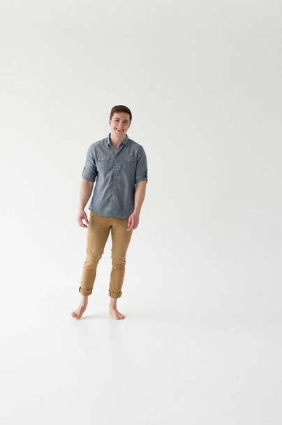 Young handsome man of strong athletic build, dressed in a shirt and brown trousers, Posing on white studio background - 写真・画像