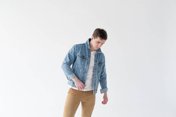 Young handsome man of strong Athlete's body, dressed in Blue jeans jacket in style of old school and brown trousers, Posing on white studio background - Photo, Image