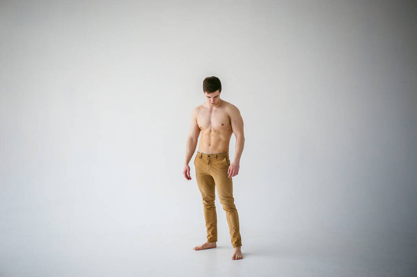 portrait young sexy handsome man of strong Athlete's body with bare torso, Dressed  brown trousers, Posing on white studio background - Photo, Image