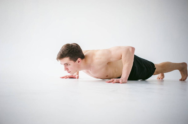 young sexy handsome men of strong Athlete's body with bare torso, Dressed black sports shorts, portrait of studio of light-skinned strong man engaged in push-ups, on floor, straining powerful hands - Foto, afbeelding