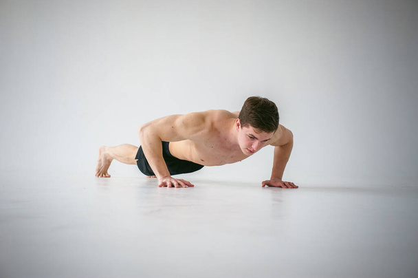 young sexy handsome men of strong Athlete's body with bare torso, Dressed black sports shorts, portrait of studio of light-skinned strong man engaged in push-ups, on floor, straining powerful hands - Photo, Image