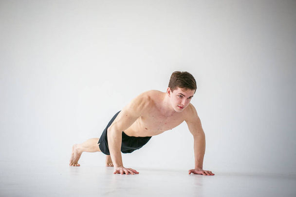 young sexy handsome men of strong Athlete's body with bare torso, Dressed black sports shorts, portrait of studio of light-skinned strong man engaged in push-ups, on floor, straining powerful hands - Photo, Image