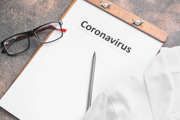 Paper sheet with text "Coronavirus" and medical uniform on grey background - Fotoğraf, Görsel