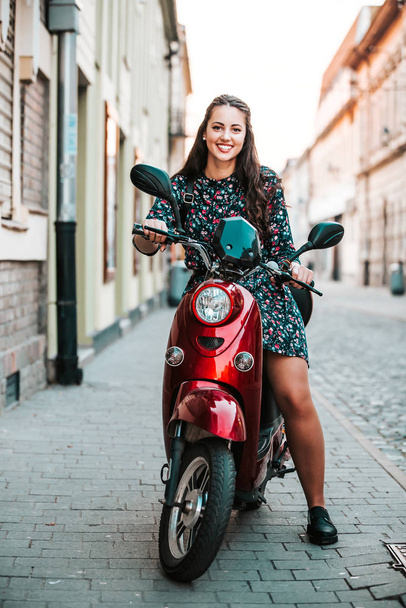 Happy cheerful girl driving scooter through city street. - Фото, зображення