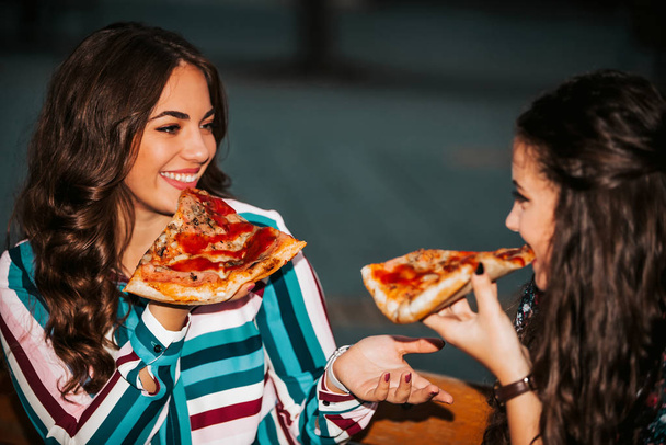 Muotokuva kaksi nuorta hymyilevää naista syö pizzaa ulkona, havin
 - Valokuva, kuva