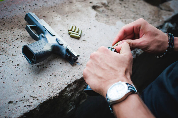 Man charges clip of pistol with bullets. Photo hands of paramilitary, reloading weapons. Preparation for shooting - 写真・画像