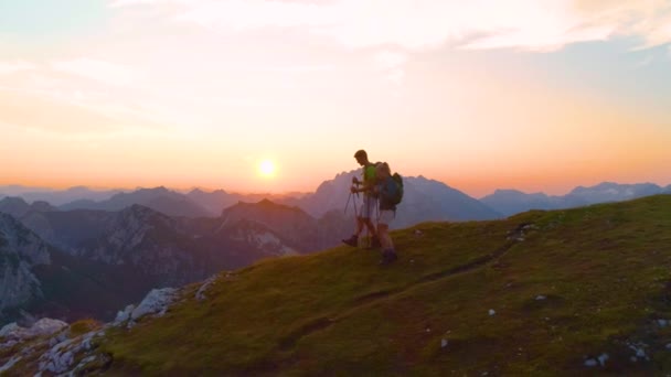AERIAL: Flying along a cheerful couple hiking down a grassy hill in the Alps. - Footage, Video